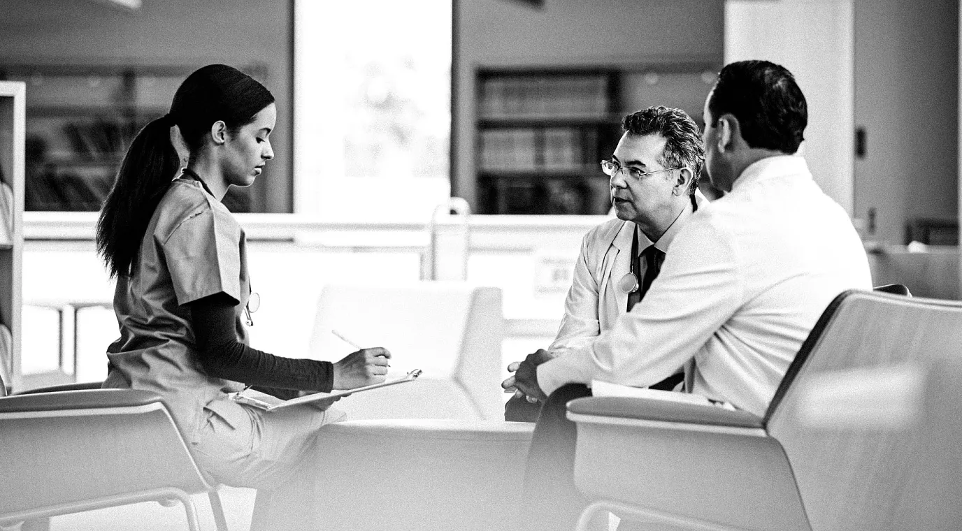 Three healthcare professionals in a hospital facility have a focused conversation.