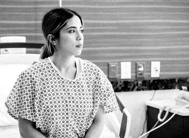 Young female patient in a hospital gown sits on a hospital bed awaiting treatment.