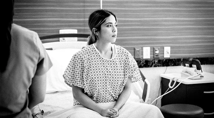 Young female patient in a hospital gown sits on a hospital bed awaiting treatment.