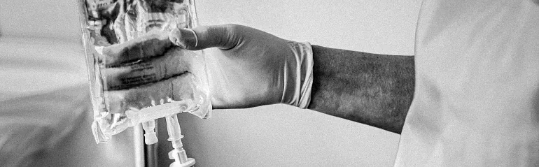A healthcare professional wearing gloves prepares an IV bag for a patient.