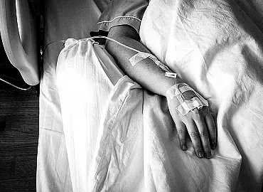 A patient lies in a hospital bed receiving treatment though an IV line.