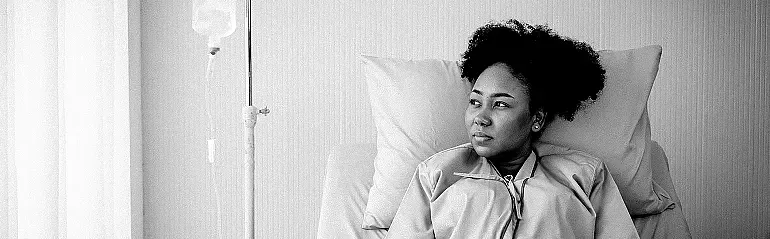 Young female patient in a hospital gown lies in a hospital bed receiving IV treatment.