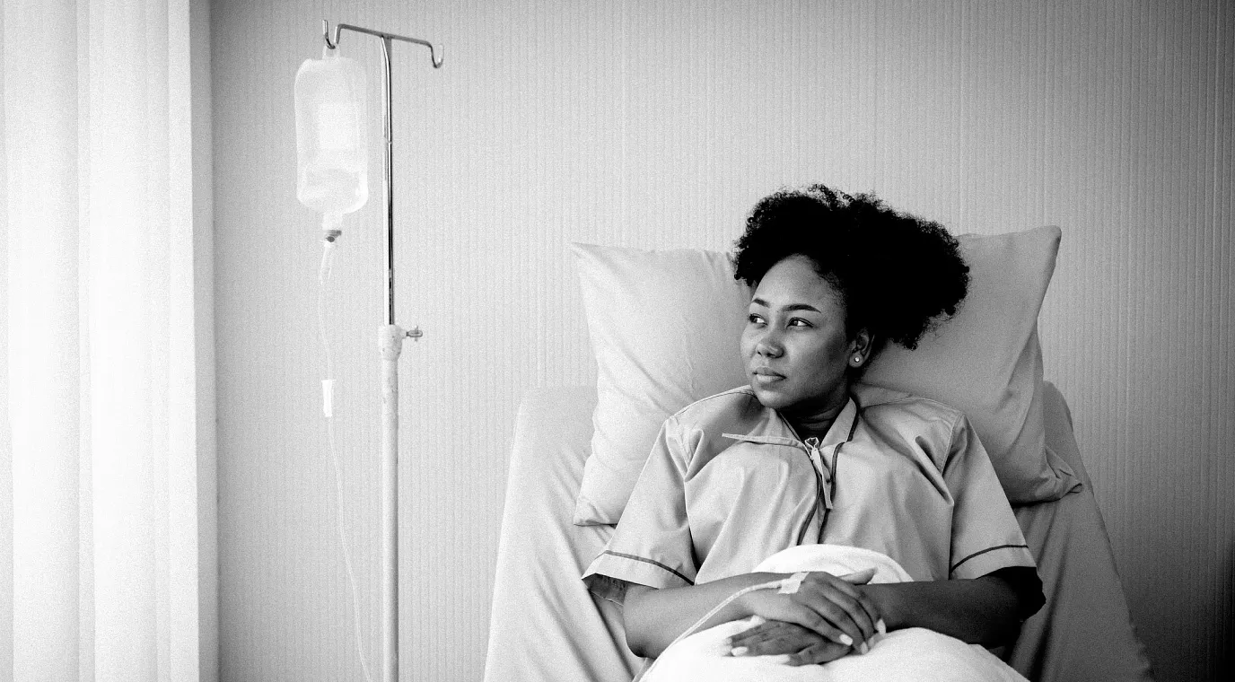 Young female patient in a hospital gown lies in a hospital bed receiving IV treatment.