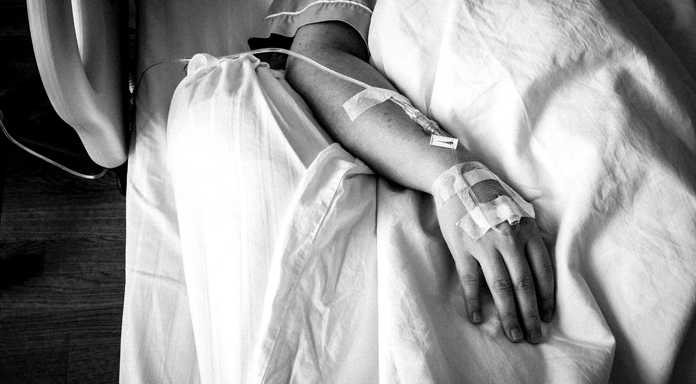 A patient lies in a hospital bed receiving treatment though an IV line.