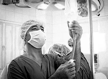 A healthcare professional wearing PPE prepares an IV bag for a patient.