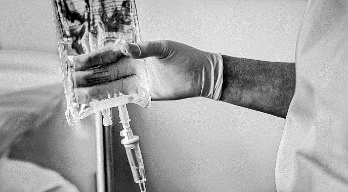 A healthcare professional wearing gloves prepares an IV bag for a patient.