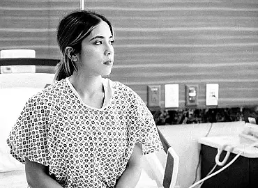 Young female patient in a hospital gown sits on a hospital bed awaiting treatment.