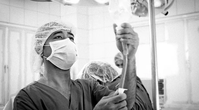 A healthcare professional wearing PPE prepares an IV bag for a patient.